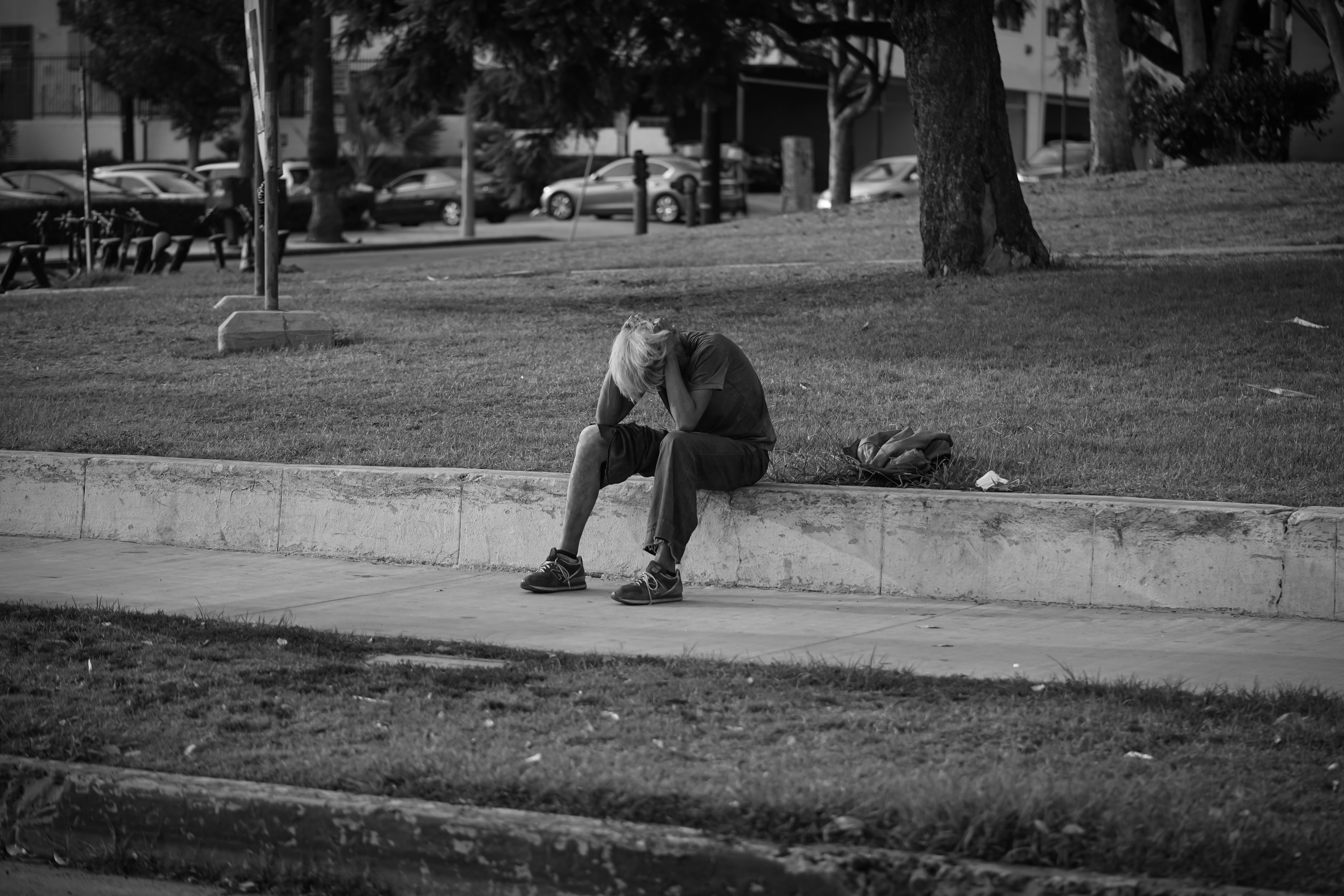 man in t-shirt and pants sitting on concrete floor in grayscale photography