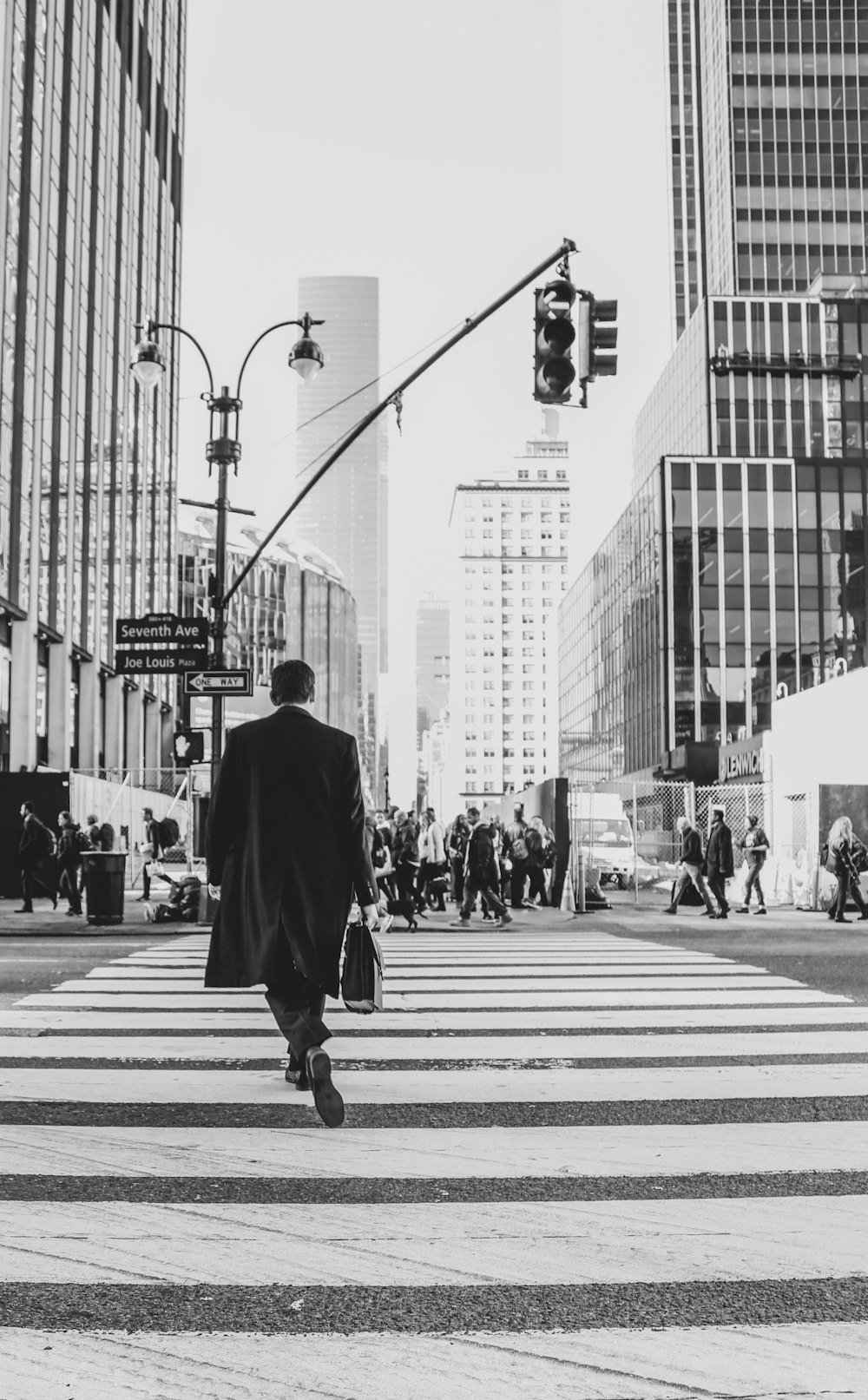 man in black coat walking on pedestrian lane in grayscale photography