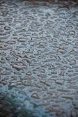 Surface covered with numerous water droplets forming irregular patterns. The droplets are clear and reflective, creating a textured appearance against a slightly blurred background.