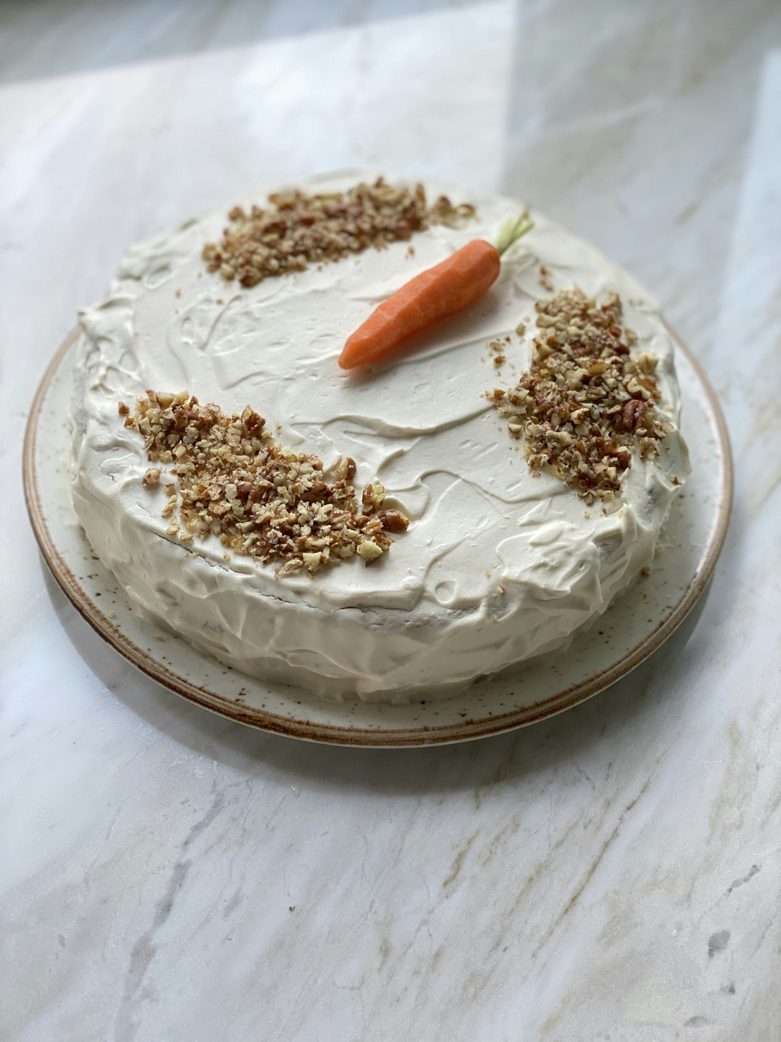Rustic naked carrot cake with cream cheese frosting and walnuts on wooden cake stand