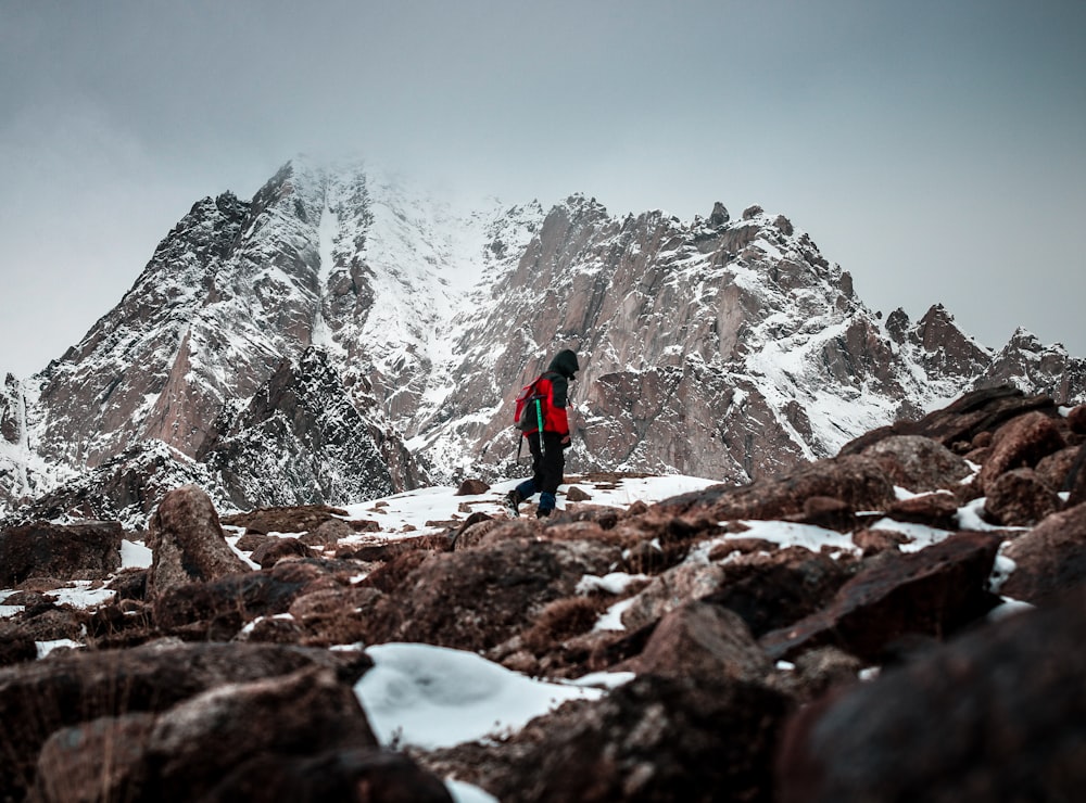 person in blue jacket and black pants standing on rocky mountain during daytime