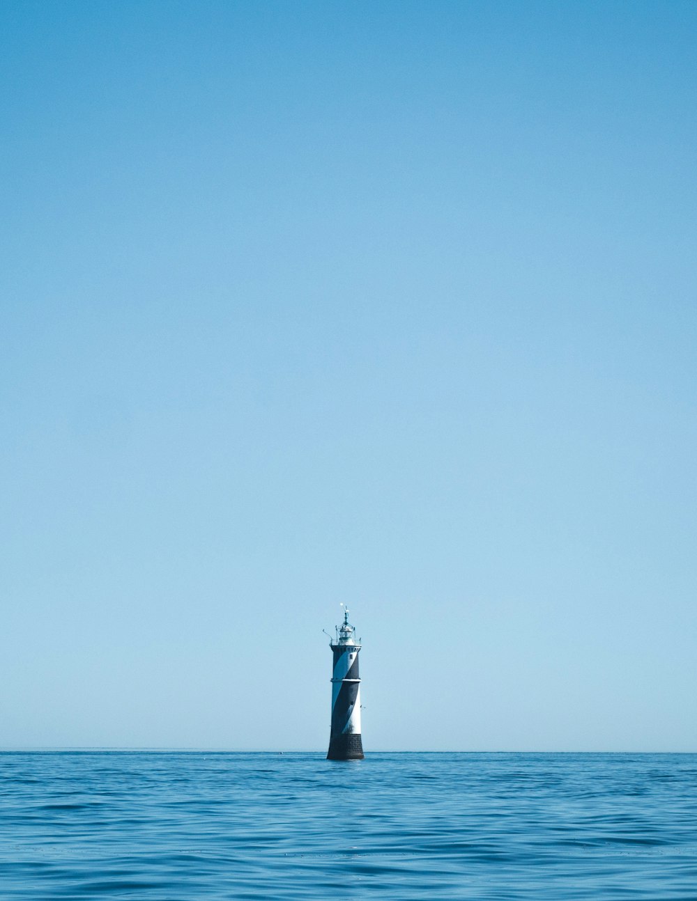 昼間の青空の下の海に浮かぶ白と黒の灯台