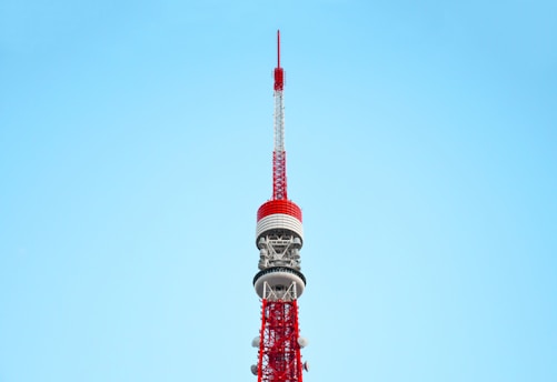 A tall, red and white communications tower against a clear blue sky. The tower features intricate metalwork and multiple antennae, demonstrating its role as a broadcasting or observation tower.