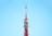 A tall, red and white communications tower against a clear blue sky. The tower features intricate metalwork and multiple antennae, demonstrating its role as a broadcasting or observation tower.