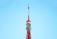 A tall, red and white communications tower against a clear blue sky. The tower features intricate metalwork and multiple antennae, demonstrating its role as a broadcasting or observation tower.