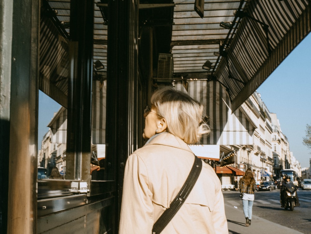 woman in beige coat standing near glass window