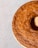 A golden-brown bundt cake with a textured surface is placed on a light speckled background. The cake has a smooth, uniform color and appears freshly baked, with a shine indicating a moist crumb.