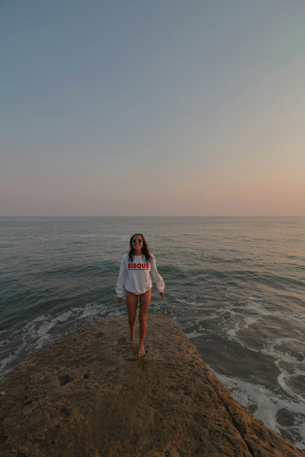 woman in white shirt standing on brown rock near body of water during daytime