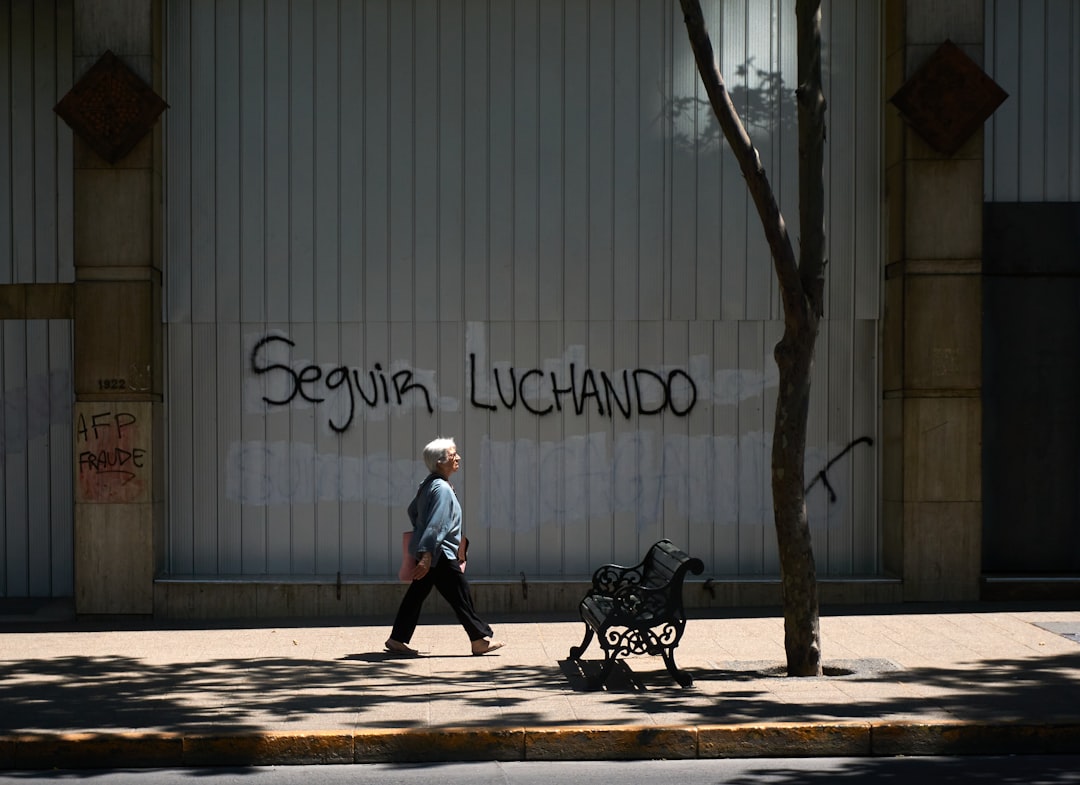 man in white shirt and black pants walking on sidewalk near wall with graffiti during daytime