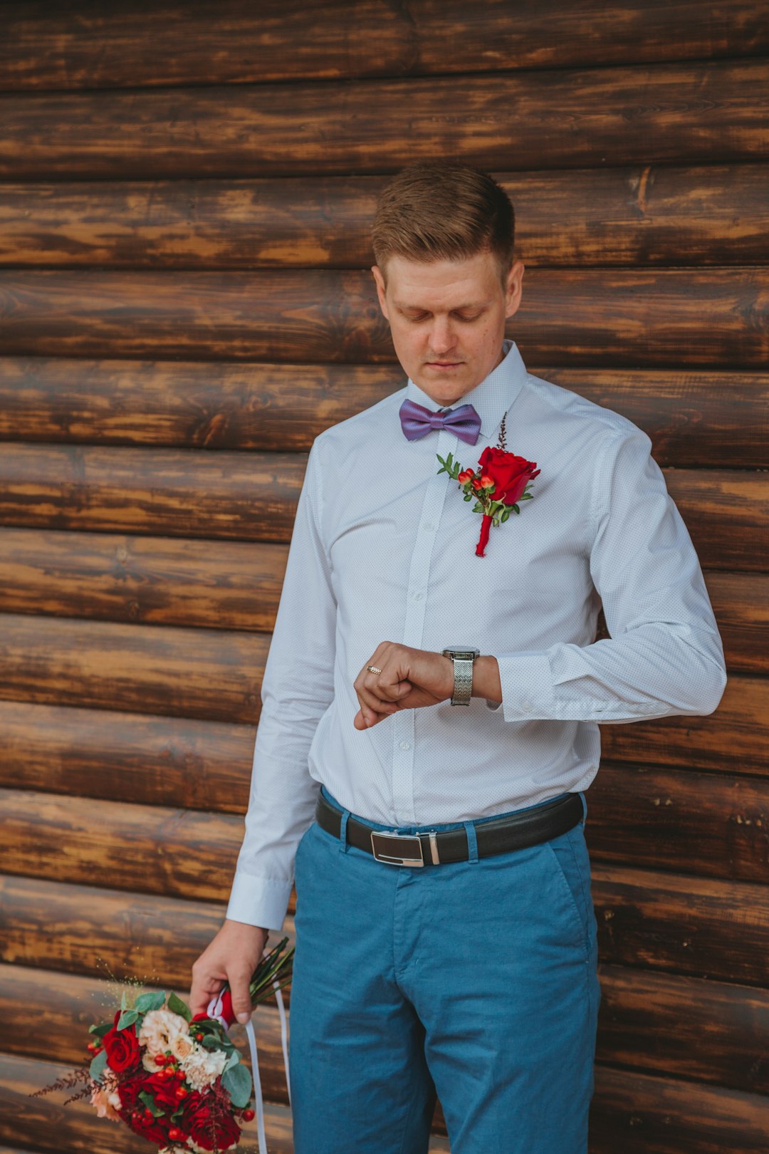 man in white dress shirt and blue denim jeans holding red rose