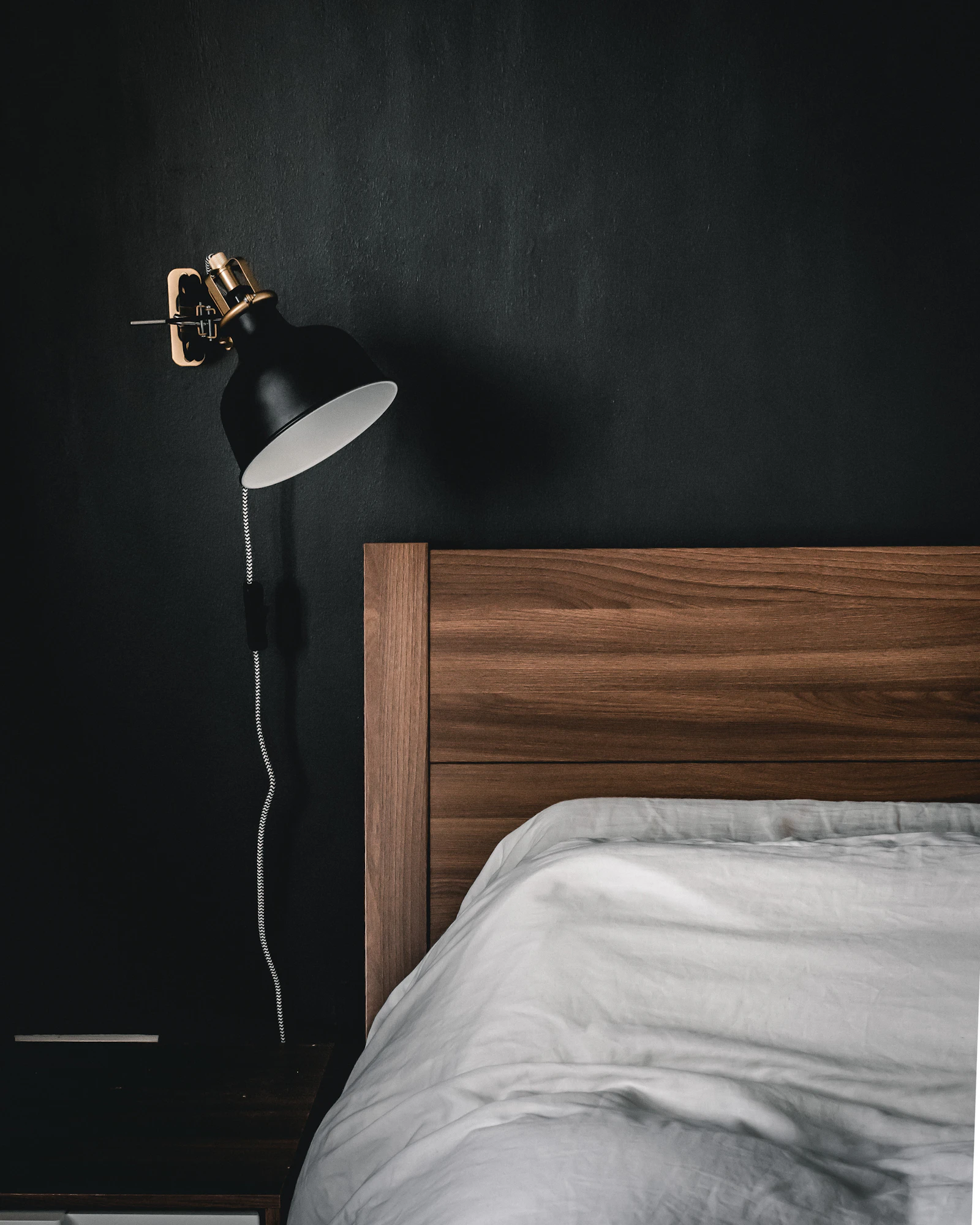 Tête de lit en bois clair contre un mur foncé, avec une applique et une literie blanche