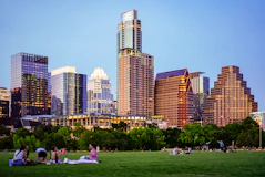 people sitting on green grass field near city buildings during daytime