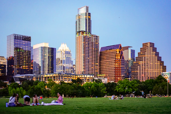 People sitting on green grass at Zilker Park with Austin skyline