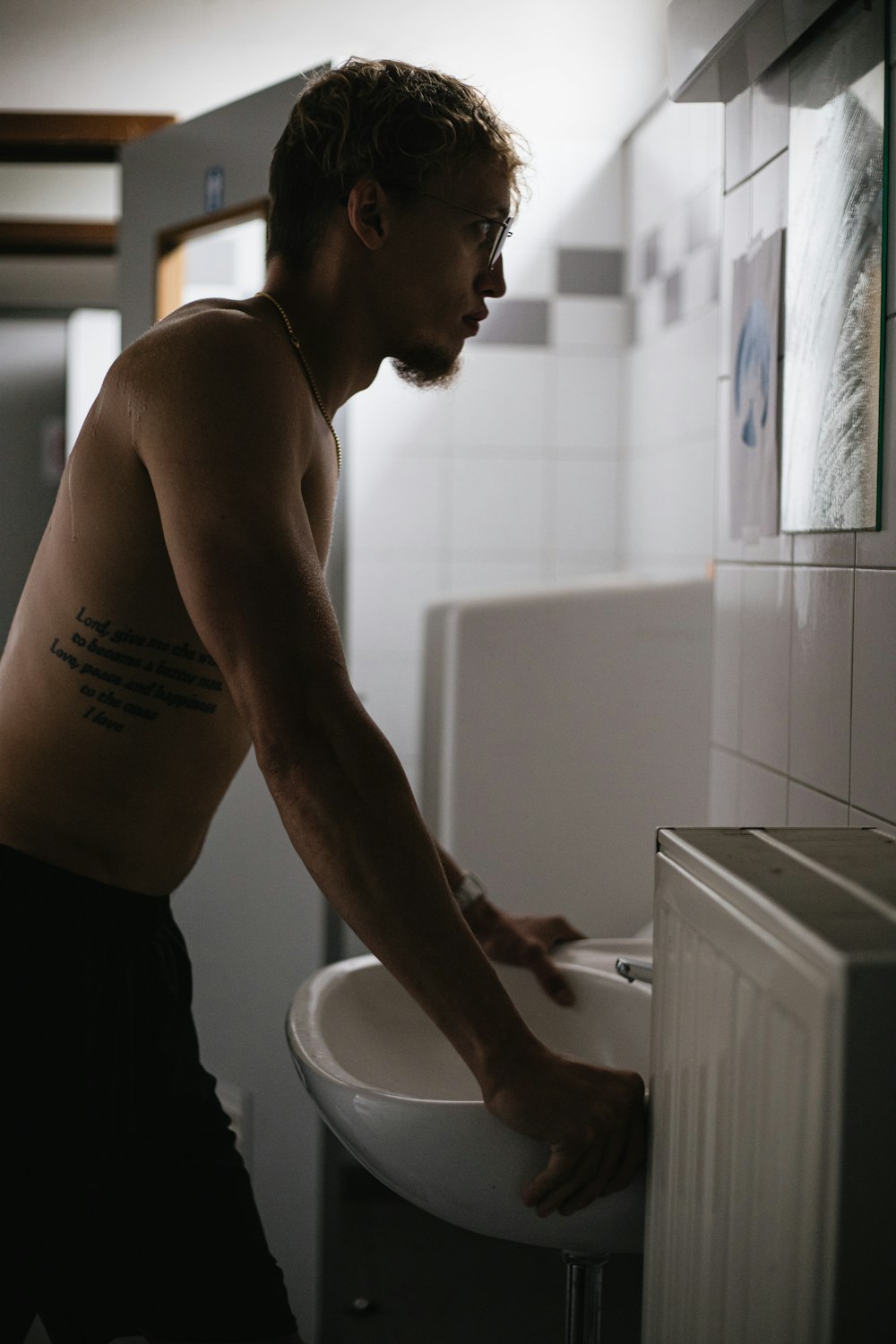 topless man in black shorts standing in front of white ceramic sink