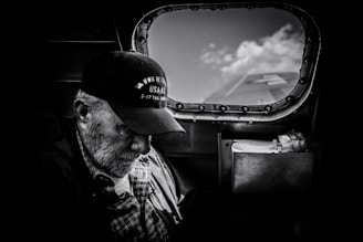 grayscale photo of man in plaid shirt and cap looking at the sky