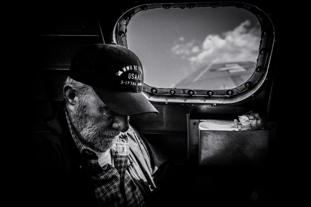 Photo en niveaux de gris d’un homme en chemise à carreaux et casquette regardant le ciel