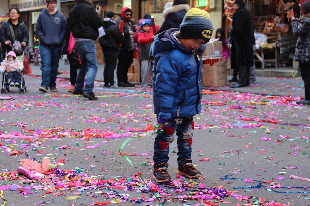 boy in black jacket walking on street with people during daytime