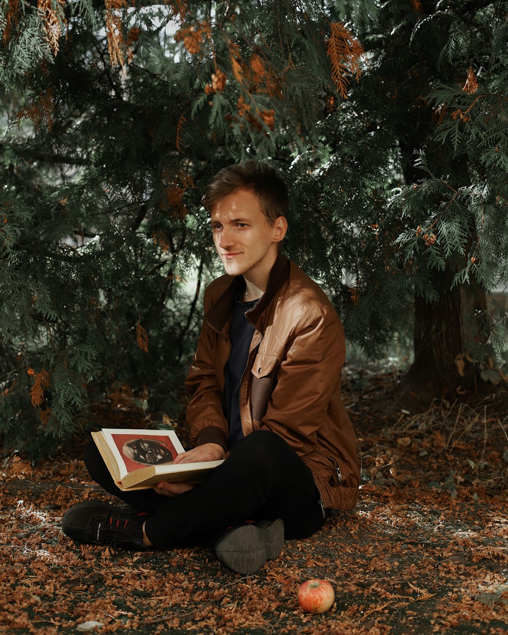 Femme en veste en cuir marron assise sur le sol avec un livre blanc