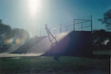 Close-up of a Sentra Skate deck as a rider launches off a ramp under bright sunlight.