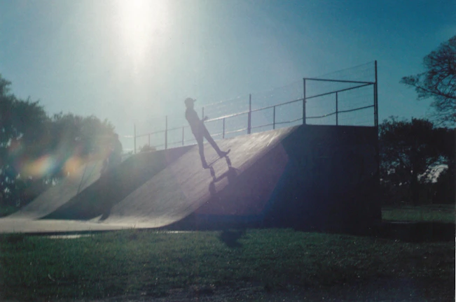 Close-up of a Sentra Skate deck as a rider launches off a ramp under bright sunlight.