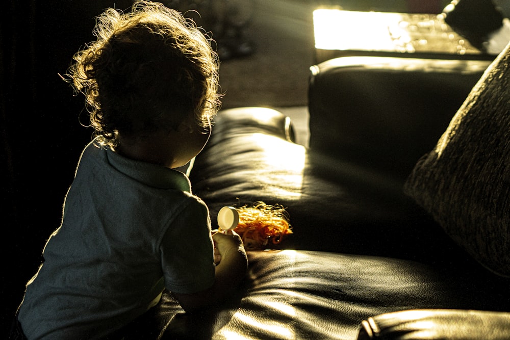 child in blue long sleeve shirt sitting on brown couch
