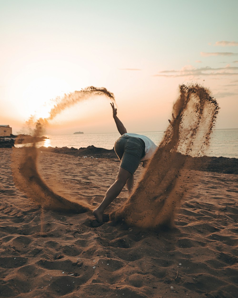 woman in black tank top and blue denim shorts sitting on brown sand during daytime