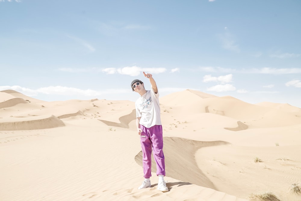 woman in white t-shirt and purple pants standing on brown sand during daytime