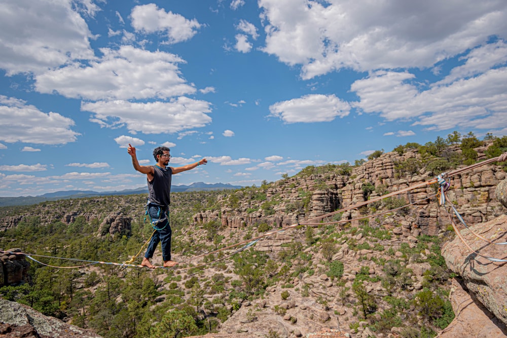 man in black t-shirt and blue denim jeans standing on rock formation under blue and