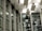 A modern architectural interior with large glass windows and a ceiling featuring rectangular light panels. The design includes a pattern of horizontal and vertical lines, creating a structured and geometric appearance.