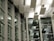A modern architectural interior with large glass windows and a ceiling featuring rectangular light panels. The design includes a pattern of horizontal and vertical lines, creating a structured and geometric appearance.