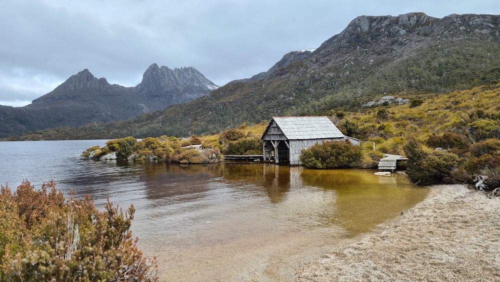 casa de madeira marrom no lago perto das montanhas durante o dia