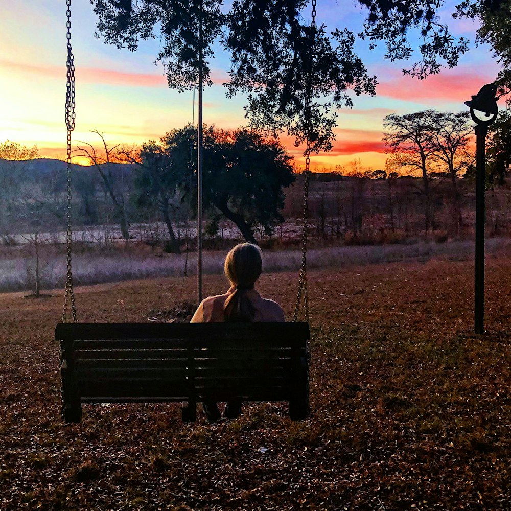 silhouette of person sitting on swing during sunset
