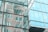 Reflective glass façade of a modern building shows abstract reflections of surrounding structures. The windows create a mirrored effect, including curved and linear architectural details.