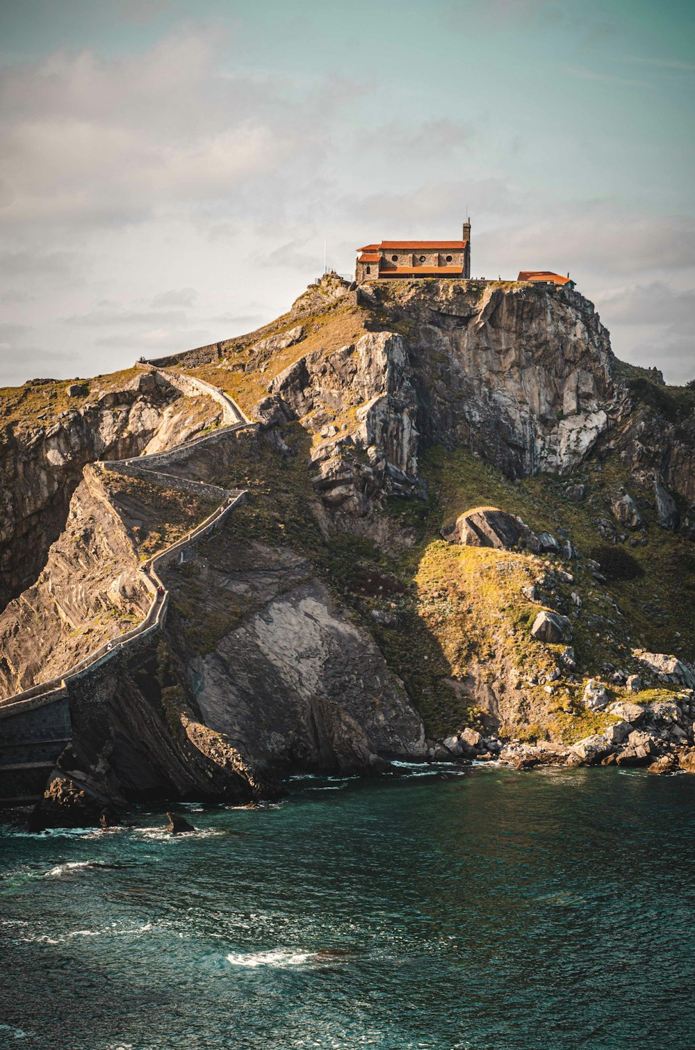 brown concrete building on cliff near body of water during daytime