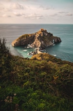 brown and green mountain beside blue sea during daytime
