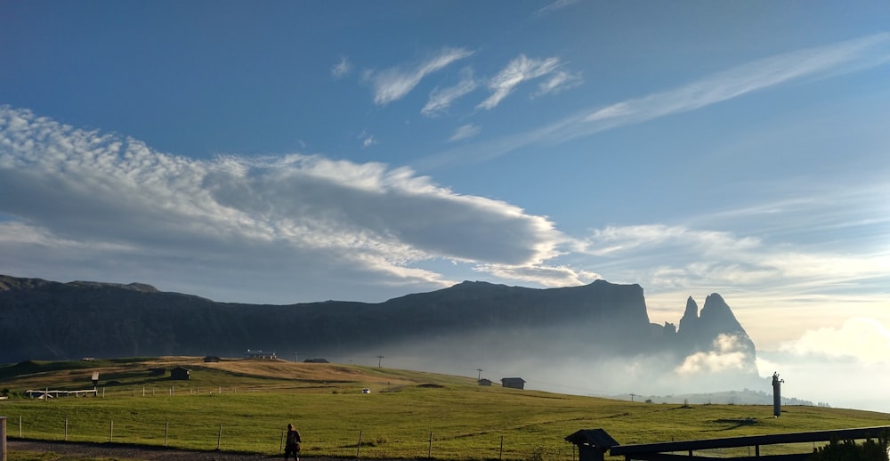 green grass field near mountain under blue sky during daytime