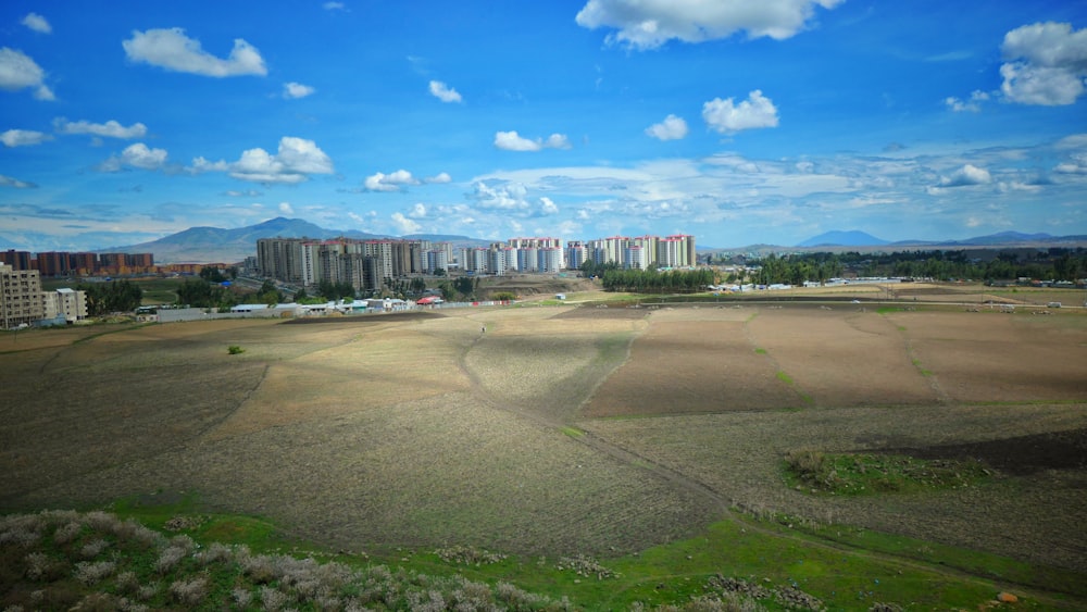 campo de grama verde perto de edifícios da cidade sob céu nublado ensolarado azul e branco durante o dia