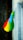 A vibrant, multicolored flag with vertical stripes of green, yellow, and red, each with a blue circle containing a yellow star in the center. It is attached to the side of a building with gray textured stone, extending outward. Below, a dark tiled walkway can be seen.
