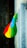A vibrant, multicolored flag with vertical stripes of green, yellow, and red, each with a blue circle containing a yellow star in the center. It is attached to the side of a building with gray textured stone, extending outward. Below, a dark tiled walkway can be seen.