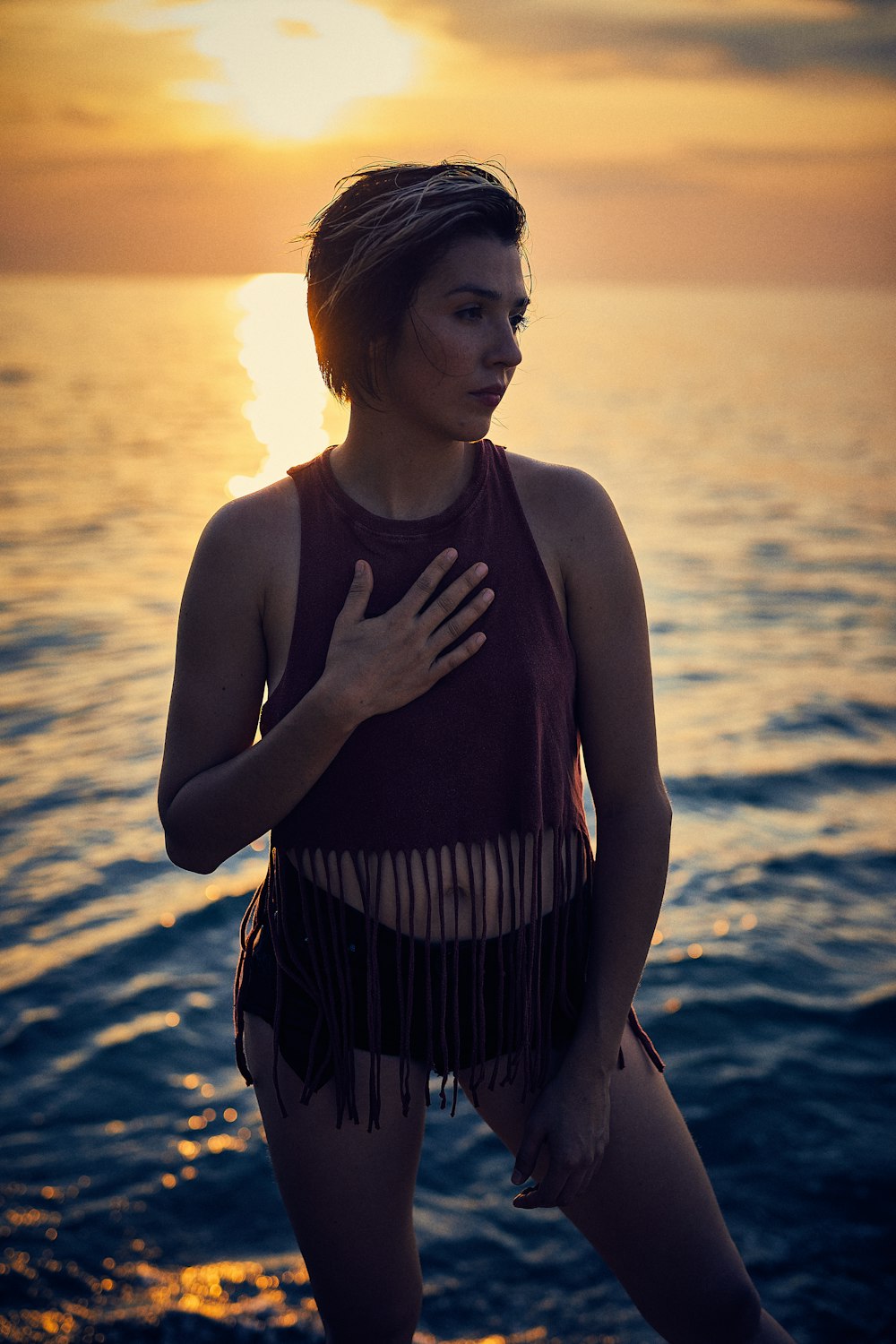 woman in black and white stripe tank top standing on seashore during sunset