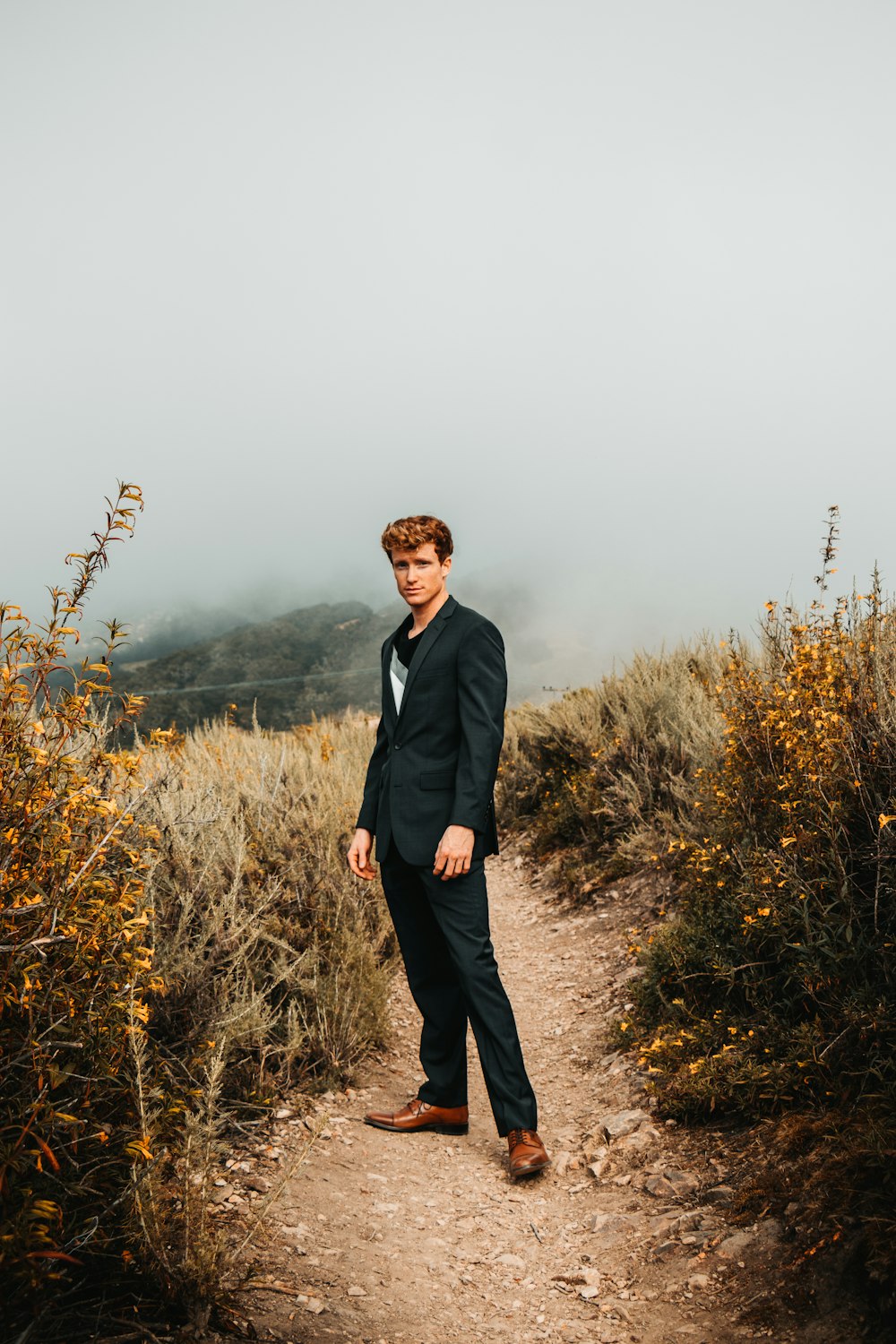 man in black suit standing on brown grass field