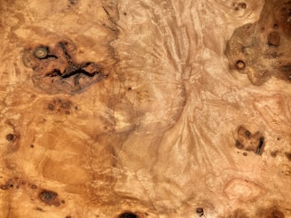 The surface is a close-up of a wooden texture with intricate grain patterns. Various knots and swirls are visible, giving it a natural, organic appearance.