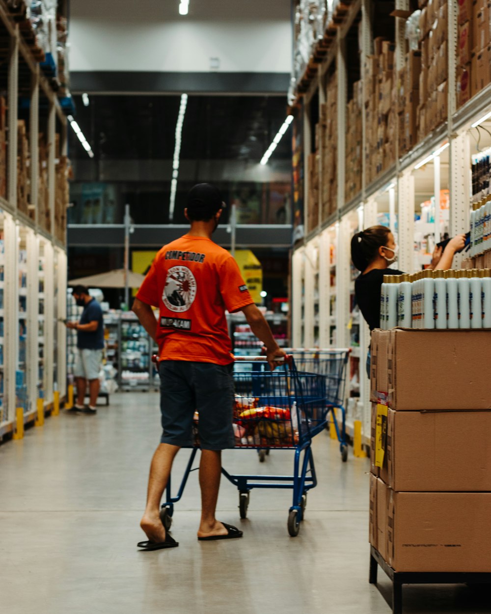 man in red crew neck t-shirt and blue denim shorts standing beside shopping cart