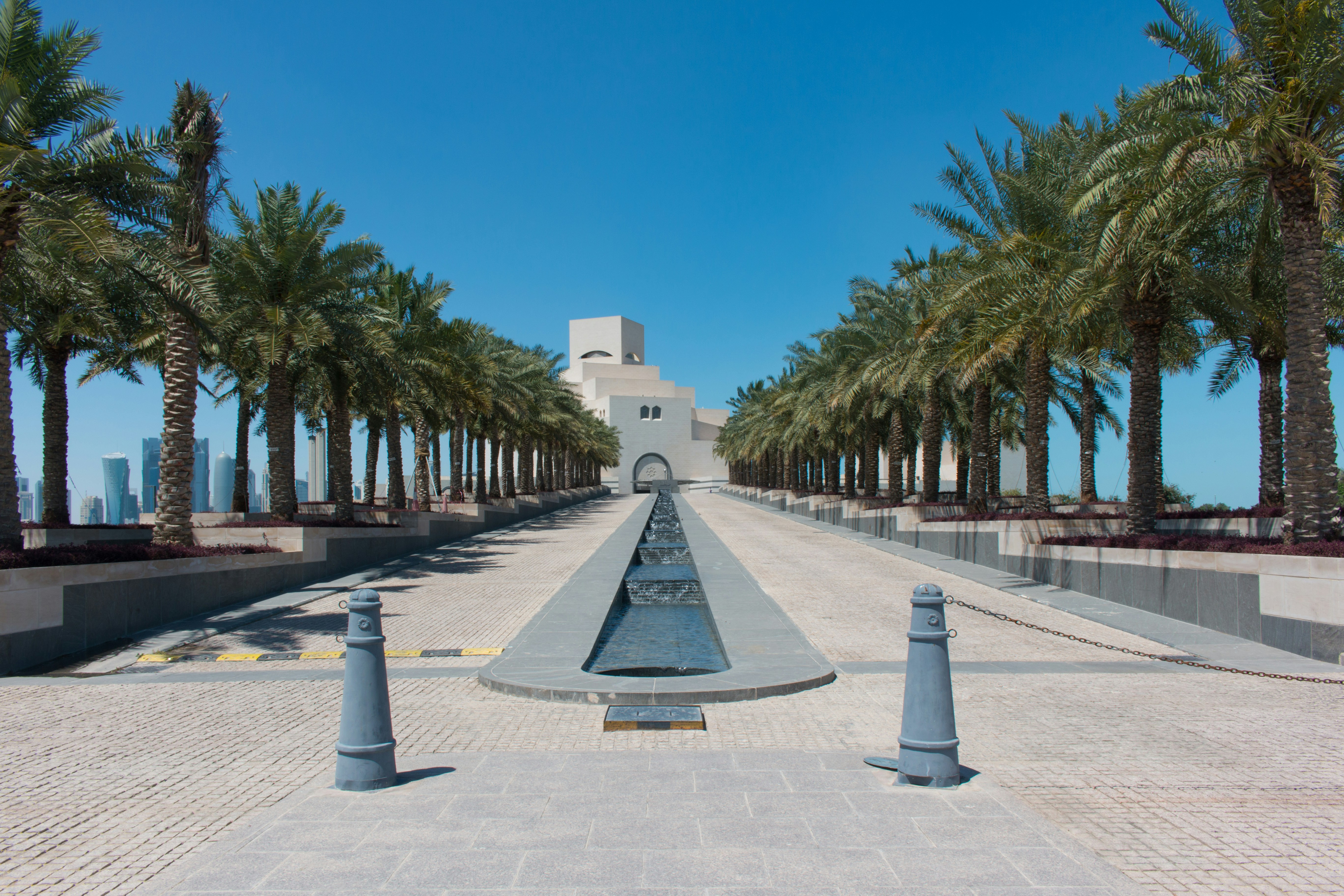 white concrete building near palm trees under blue sky during daytime, The Museum of Islamic Art is a museum on one end of the seven-kilometer-long Corniche in Doha, Qatar.