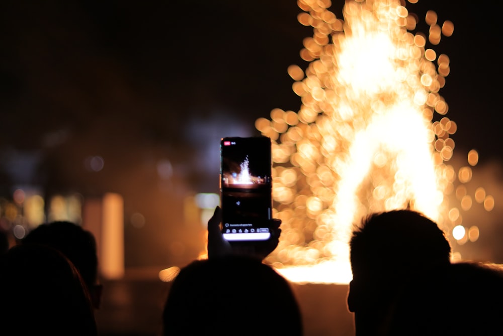 person taking photo of fire during night time