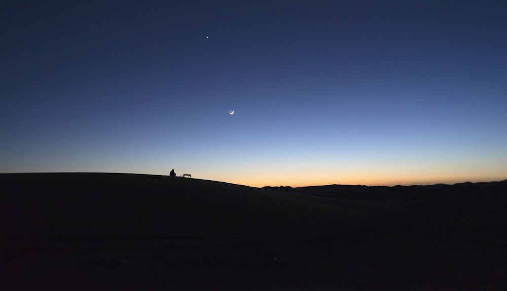 silhouette of person standing on hill during sunset