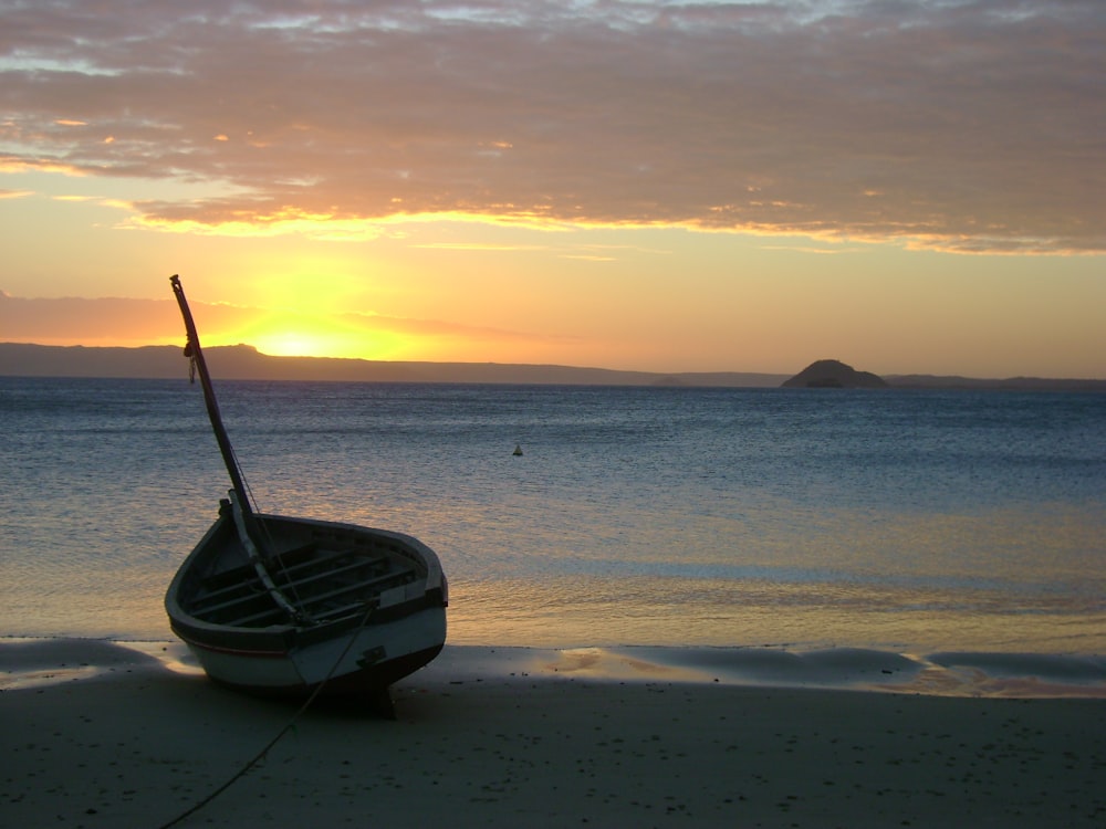 Weißes und schwarzes Boot am Strand bei Sonnenuntergang