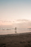 Surfer carrying a board along a rugged Baja beach at dawn.