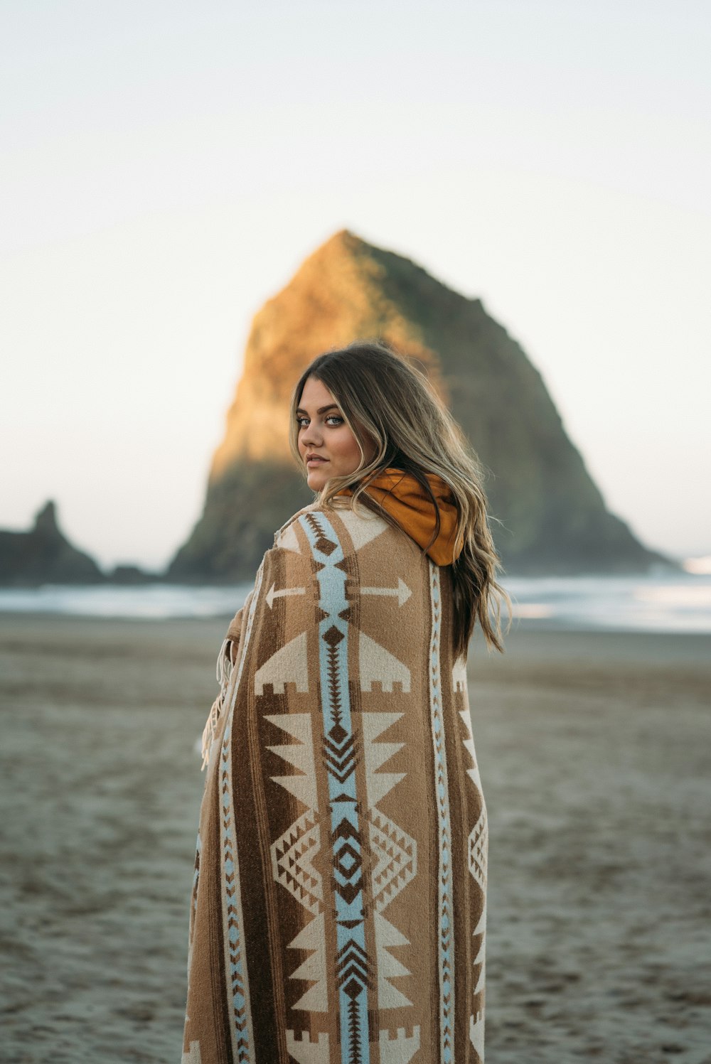 낮 동안 해변에 서 있는 갈색과 흰색 부족 까마귀를 입은 여자