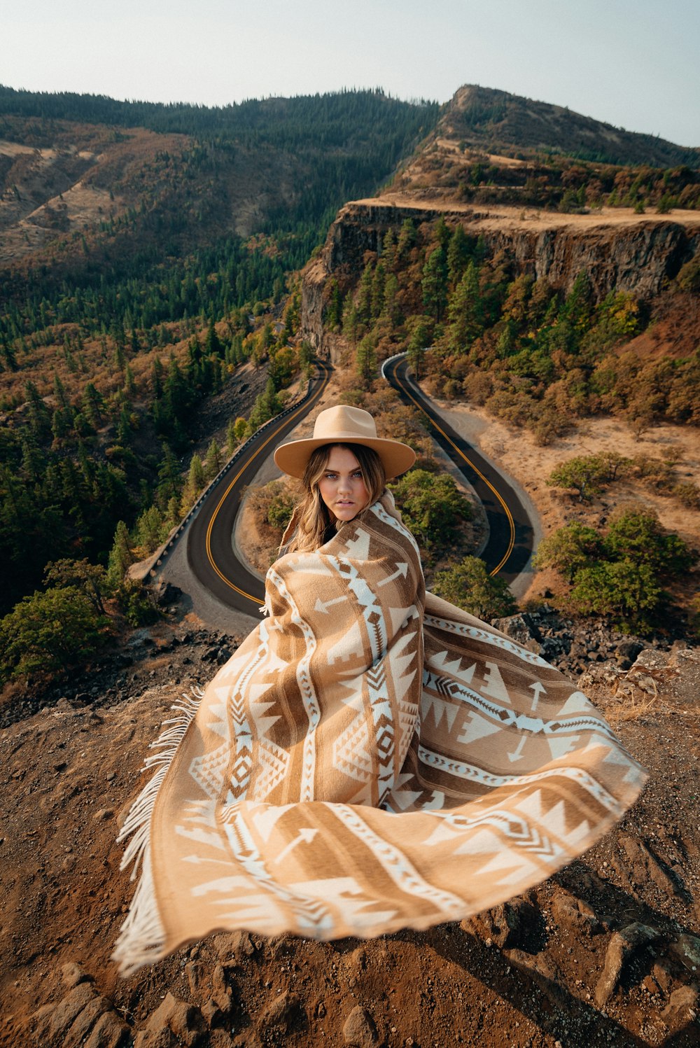 woman in brown and white floral dress wearing black hat sitting on brown rock during daytime